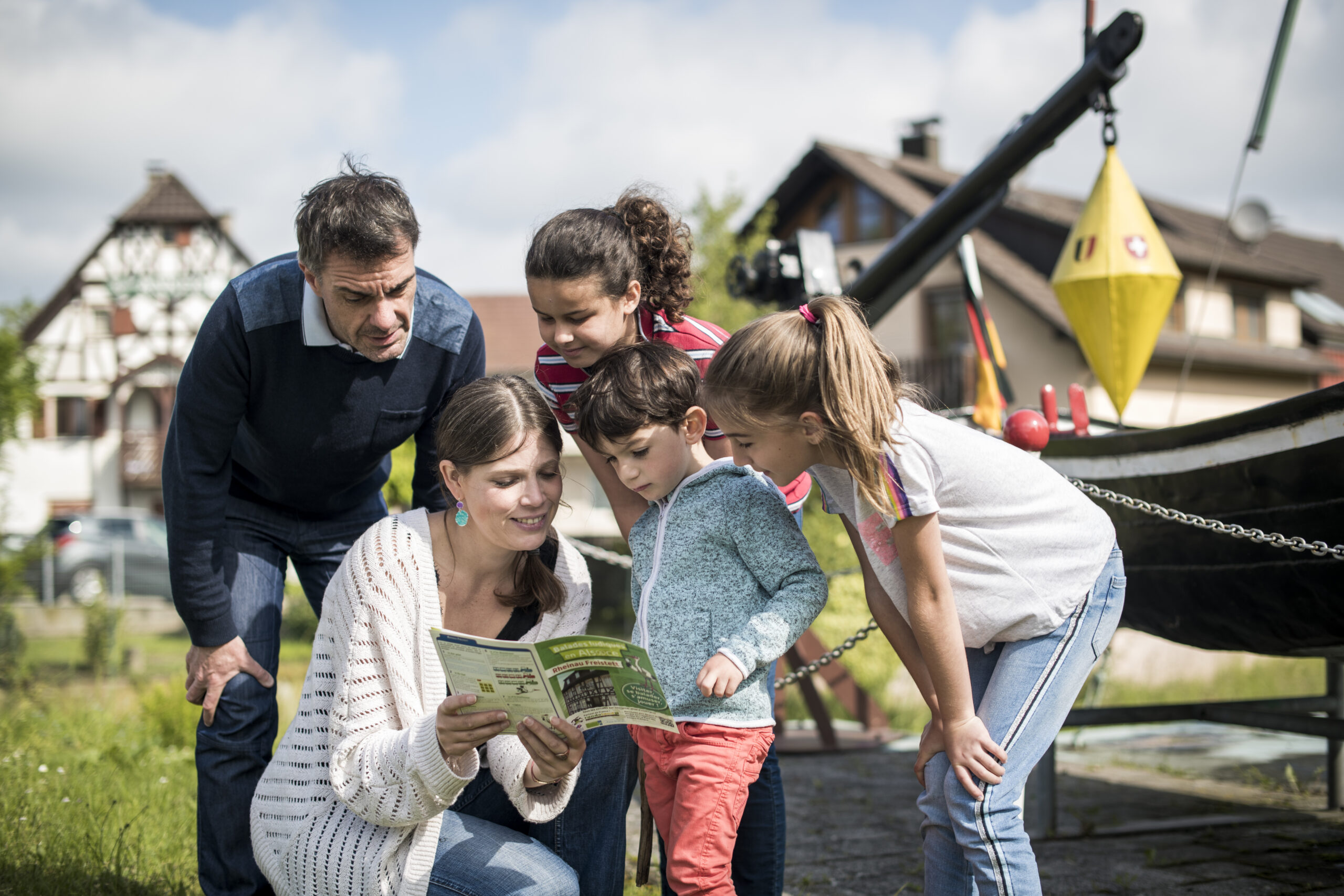Eine Familie macht die Schatzsuche in Rheinau. Die Mutter hält das Heft in den Händen, während die drei Kinder und der Vater aufmerksam lesen und zuhören.